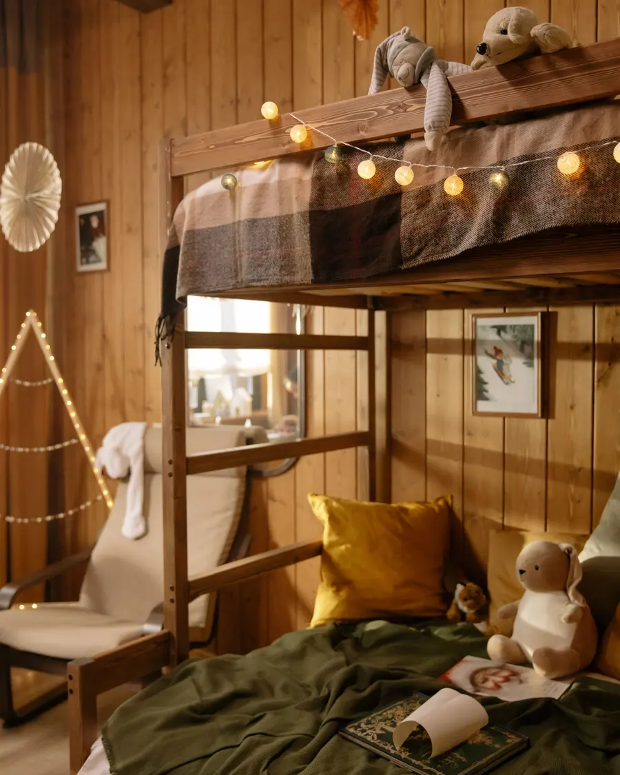 Quarto de madeira com beliche, varal de luzes, bichos de pelúcia e uma escrivaninha