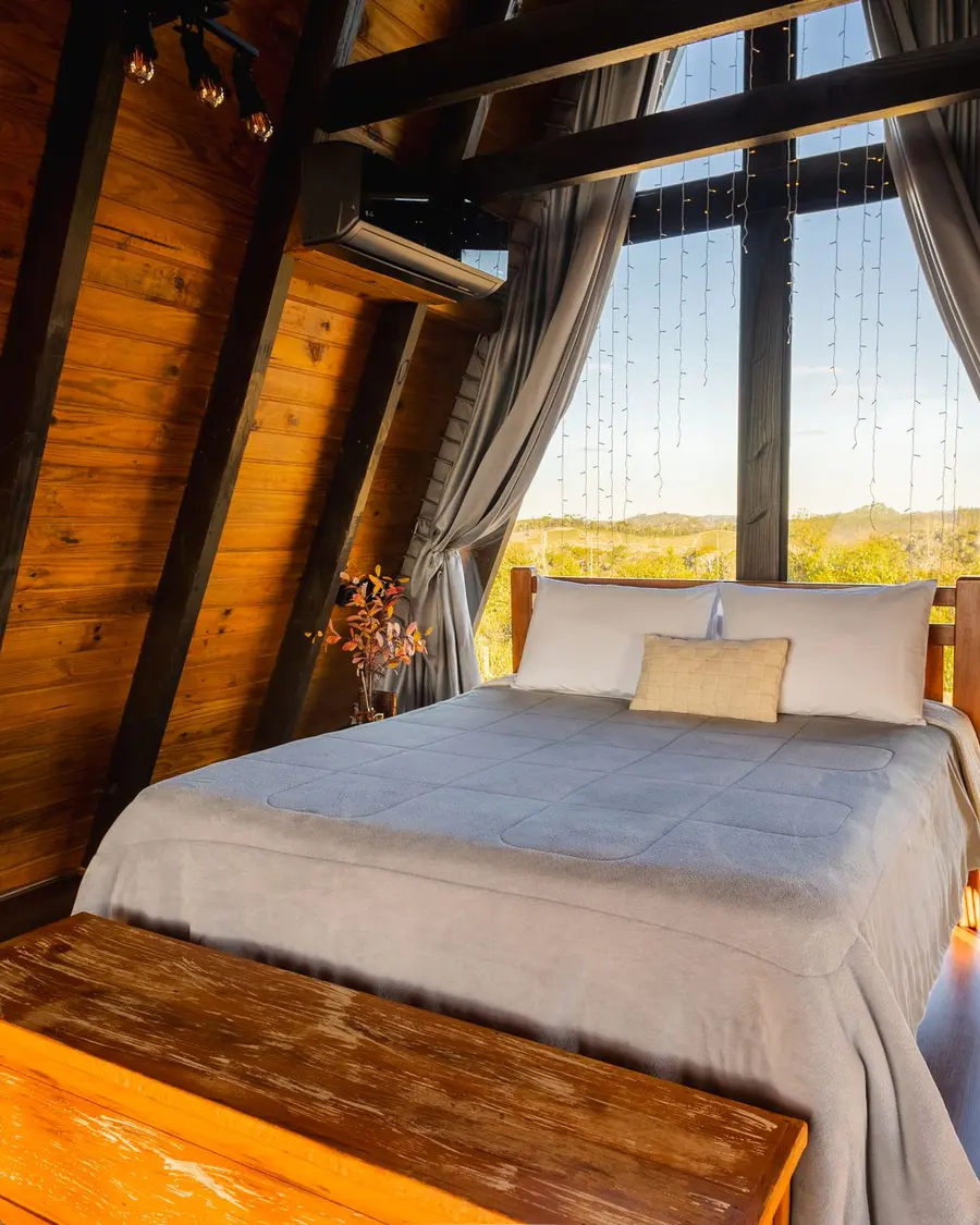 Quarto de madeira em formato de A com cama de casal virada para um janelão de vidro